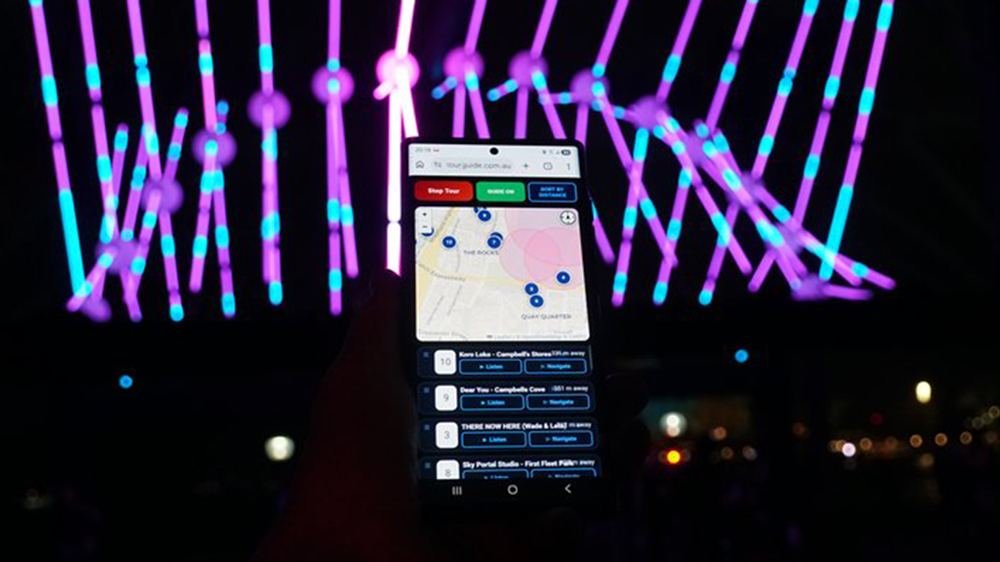 Phone running the FREE Sydney Light Walk audio guide held up against Vivid 2026 laser installations
